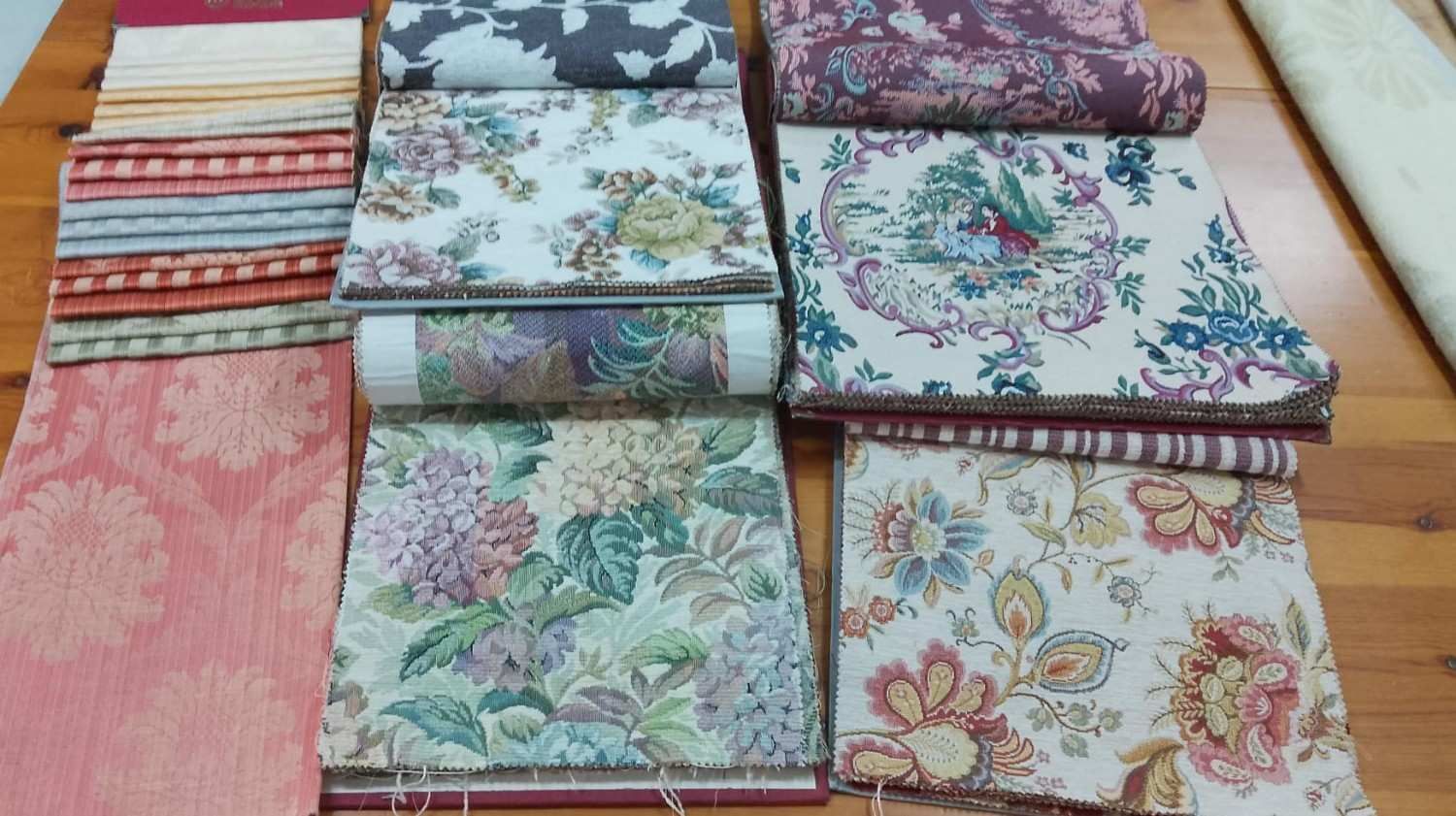 Una colección de muestras de tela con diversos estampados florales y otros diseños, dispuestas sobre una mesa de madera.