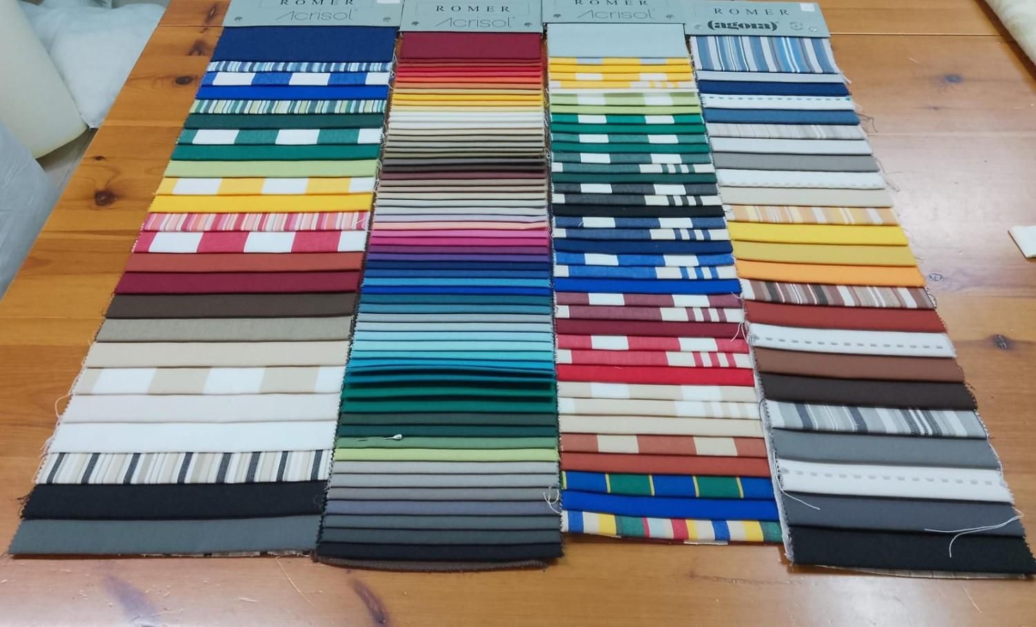 Cuatro filas verticales de muestras de tela de diversos colores, estampados y rayas, expuestas sobre una mesa de madera.