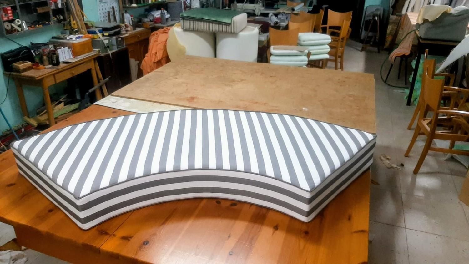 Un cojín curvo con rayas verticales grises y blancas descansa sobre un gran banco de trabajo de madera en un taller.