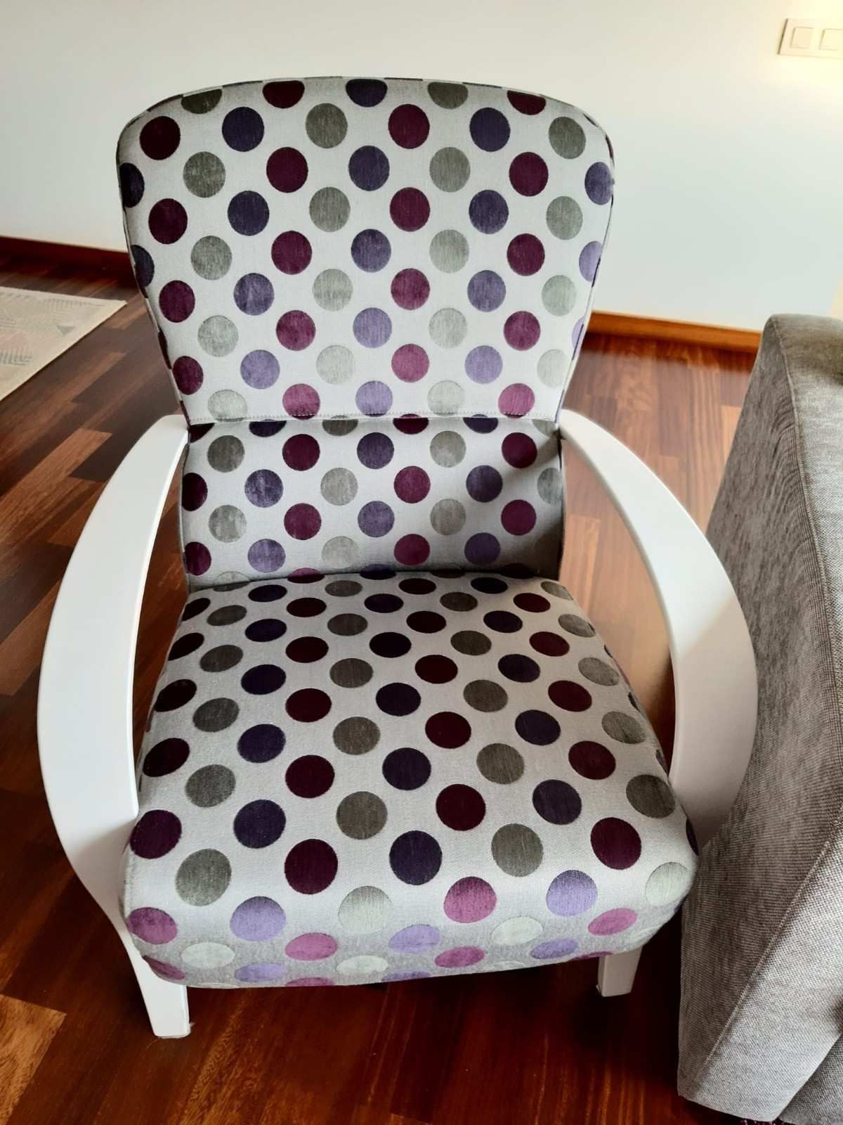 Un sillón tapizado con brazos curvos blancos y un estampado de lunares morados y grises sobre un fondo claro.