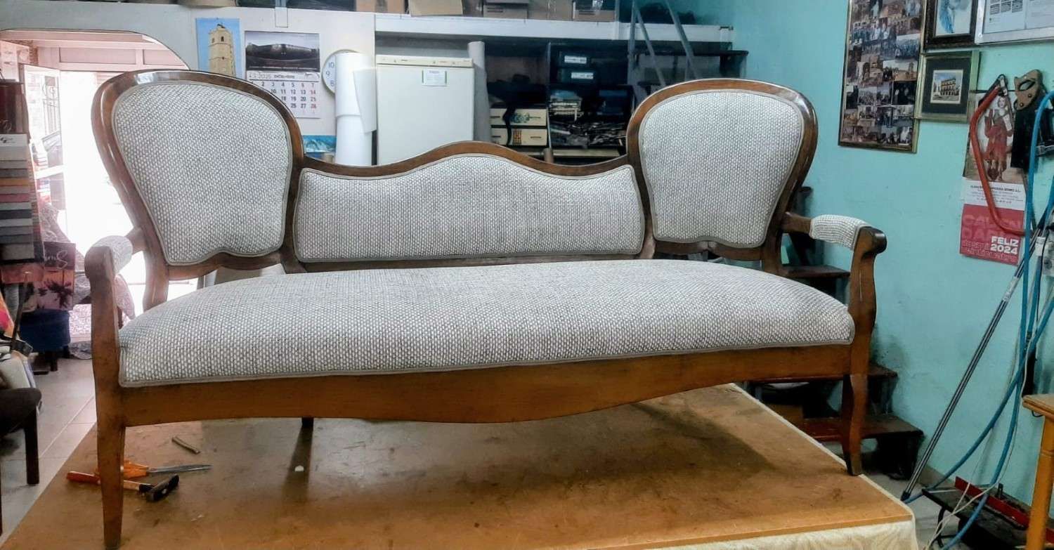 Un sofá antiguo con estructura de madera curvada y tapicería de tela estampada de color claro en un entorno de taller.