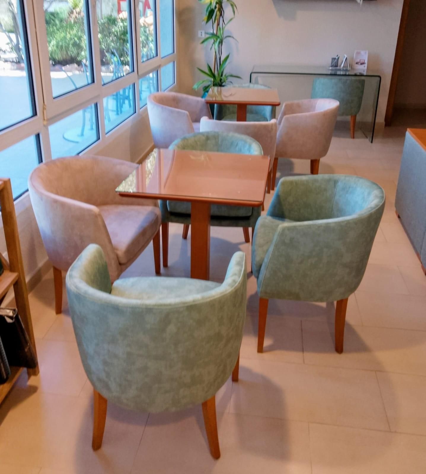 Una zona de estar con sillones tapizados en rosa claro y verde pálido, dispuestos alrededor de pequeñas mesas de madera en una habitación luminosa.