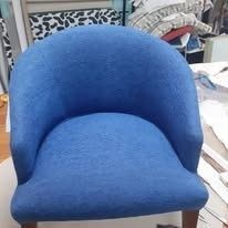 Una silla tipo barril tapizada en azul con patas de madera, vista desde el frente en una habitación.