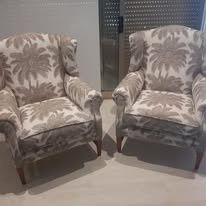 Dos sillones orejeros a juego con estampado floral en beige y blanco, colocados uno al lado del otro sobre un suelo de color claro.