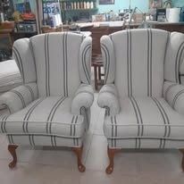 Dos sillones orejeros a juego, tapizados en tela a rayas blancas y grises y con patas de madera, en un entorno de taller.