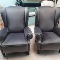 Dos sillones orejeros grises tapizados con respaldo alto están colocados uno al lado del otro sobre un suelo de color claro.