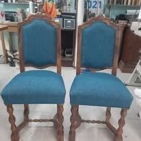 Dos sillas de comedor de madera idénticas, tapizadas en tela color turquesa y con patas torneadas, se encuentran una al lado de la otra en un taller.