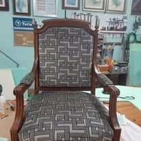 Un sillón de madera tapizado con un estampado geométrico gris y blanco en un entorno de taller.