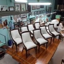 Seis sillas tapizadas en blanco con armazón de madera oscura dispuestas sobre una mesa de madera pulida en un taller.