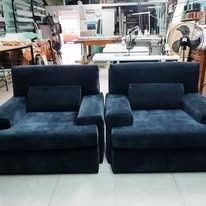 Dos sillones tapizados en azul oscuro, idénticos, colocados uno al lado del otro en un taller o tienda de muebles.
