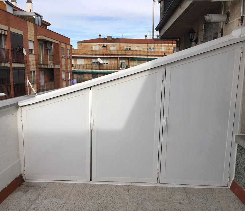 Una puerta blanca en un balcón con edificios al fondo.