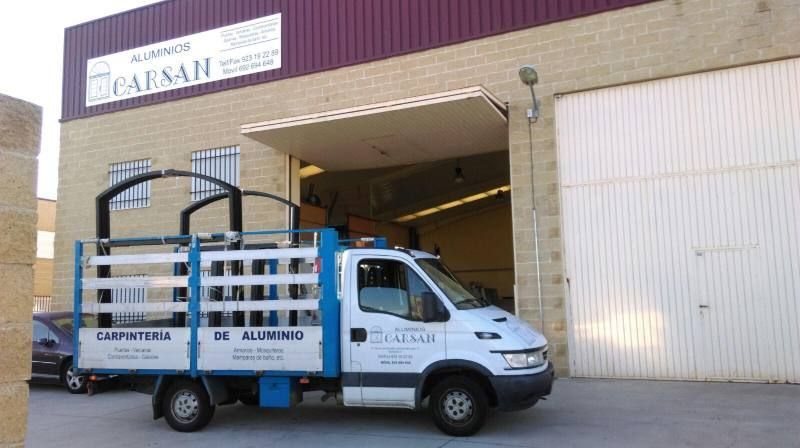 Un camión blanco y azul está estacionado frente a un edificio que dice carsan