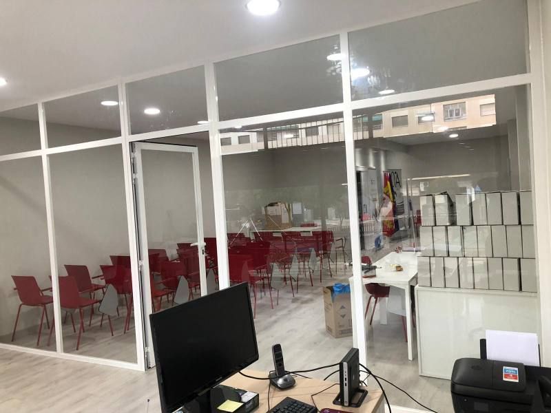 Una computadora está sobre un escritorio en una habitación con una pared de vidrio.