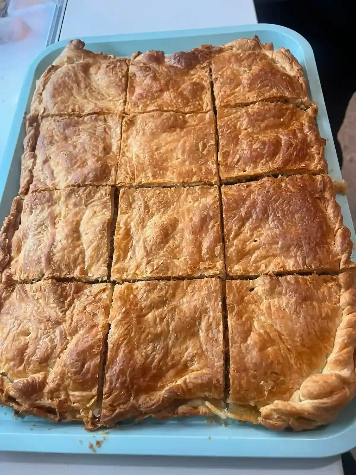 Pastel de color marrón dorado cortado en cuadrados sobre una bandeja azul, visto desde arriba.