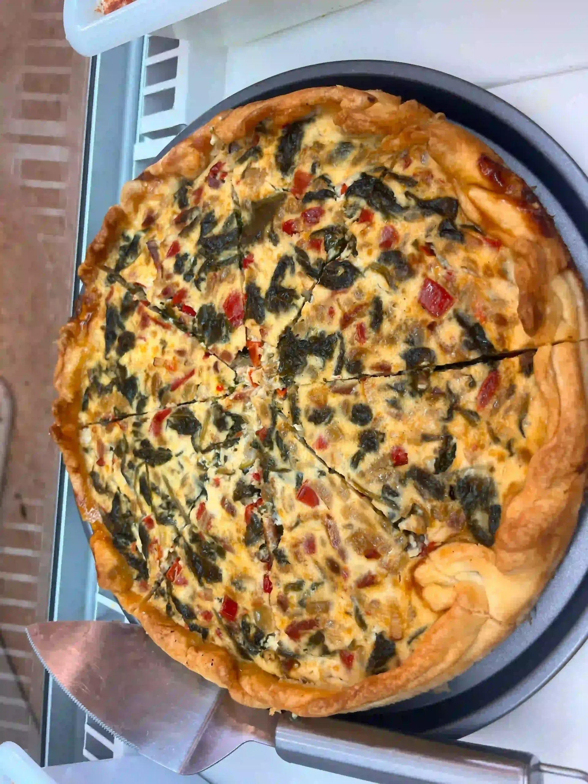 Pizza de espinacas y tomate en una bandeja, vista desde arriba.