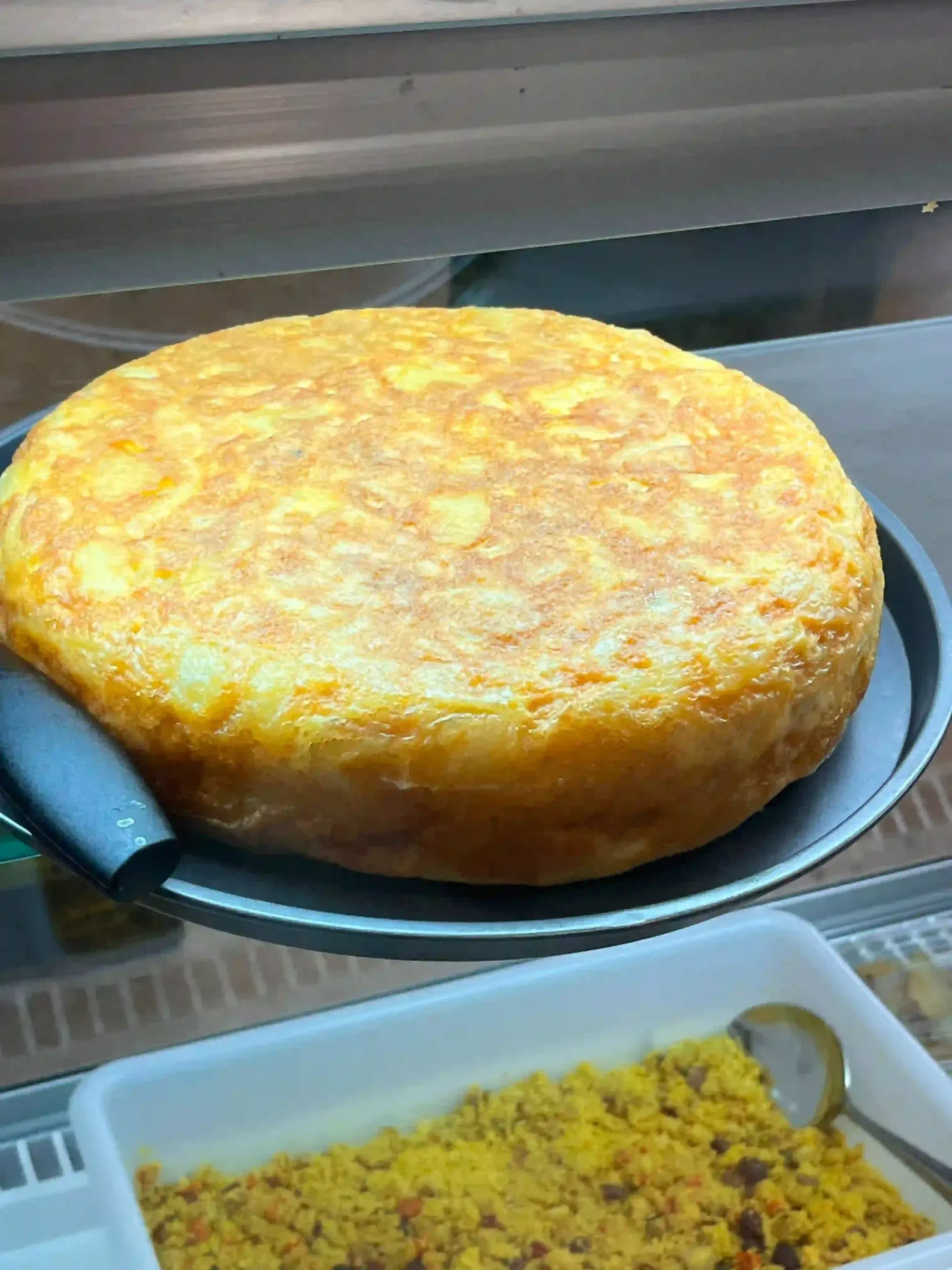 Un plato redondo dorado horneado sobre una bandeja junto a un recipiente de arroz amarillo o cuscús.