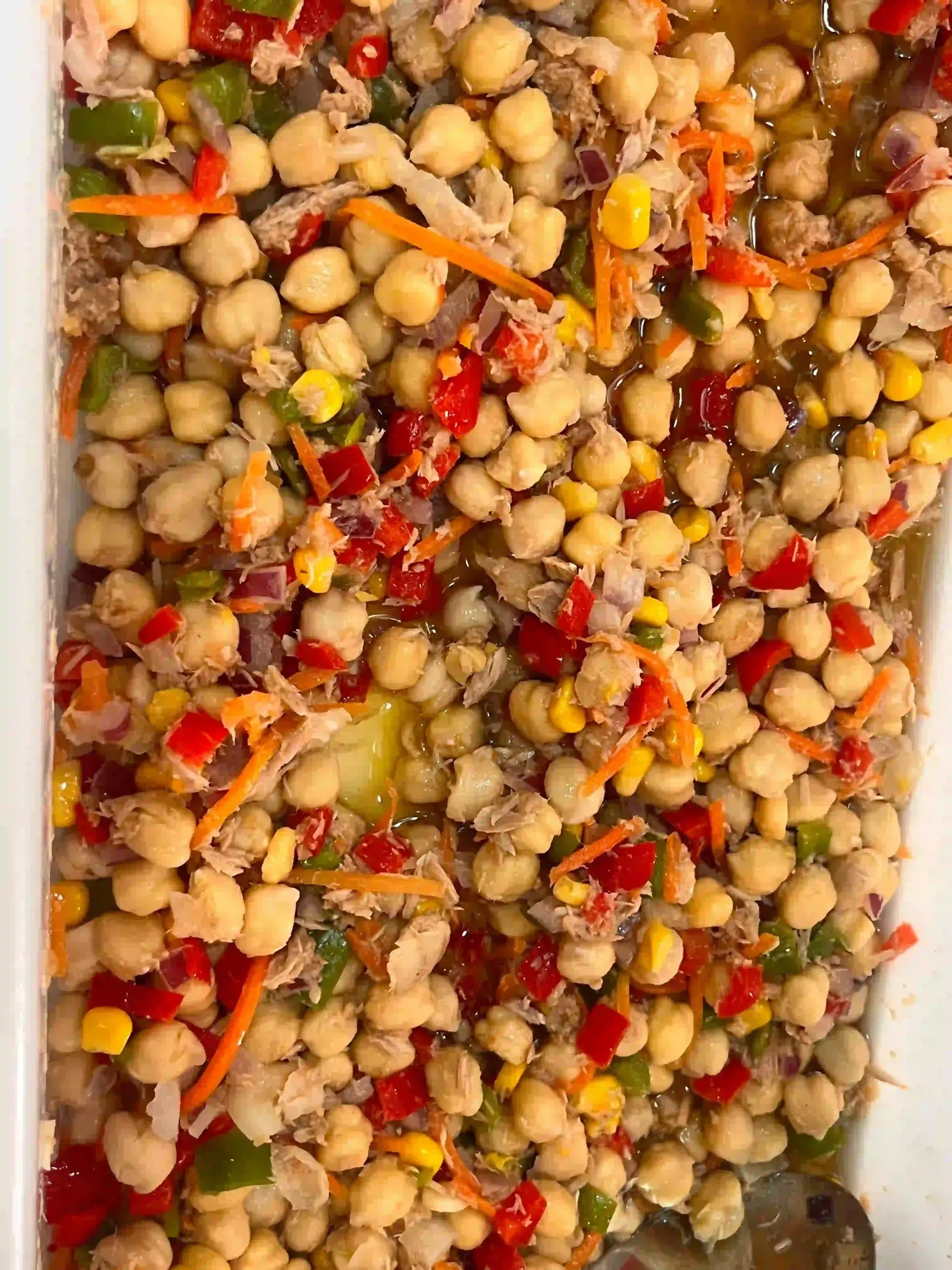 Ensalada mixta de legumbres con garbanzos, pimientos rojos, maíz y hierbas en un plato blanco.