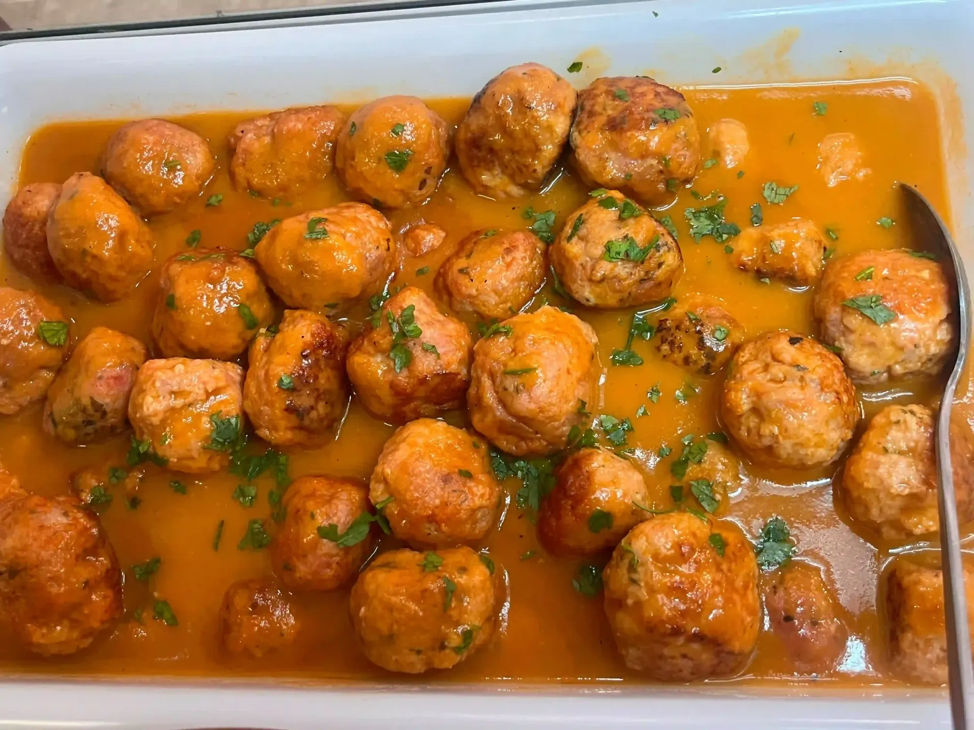 Albóndigas en salsa de naranja en un plato rectangular, adornadas con hierbas picadas.