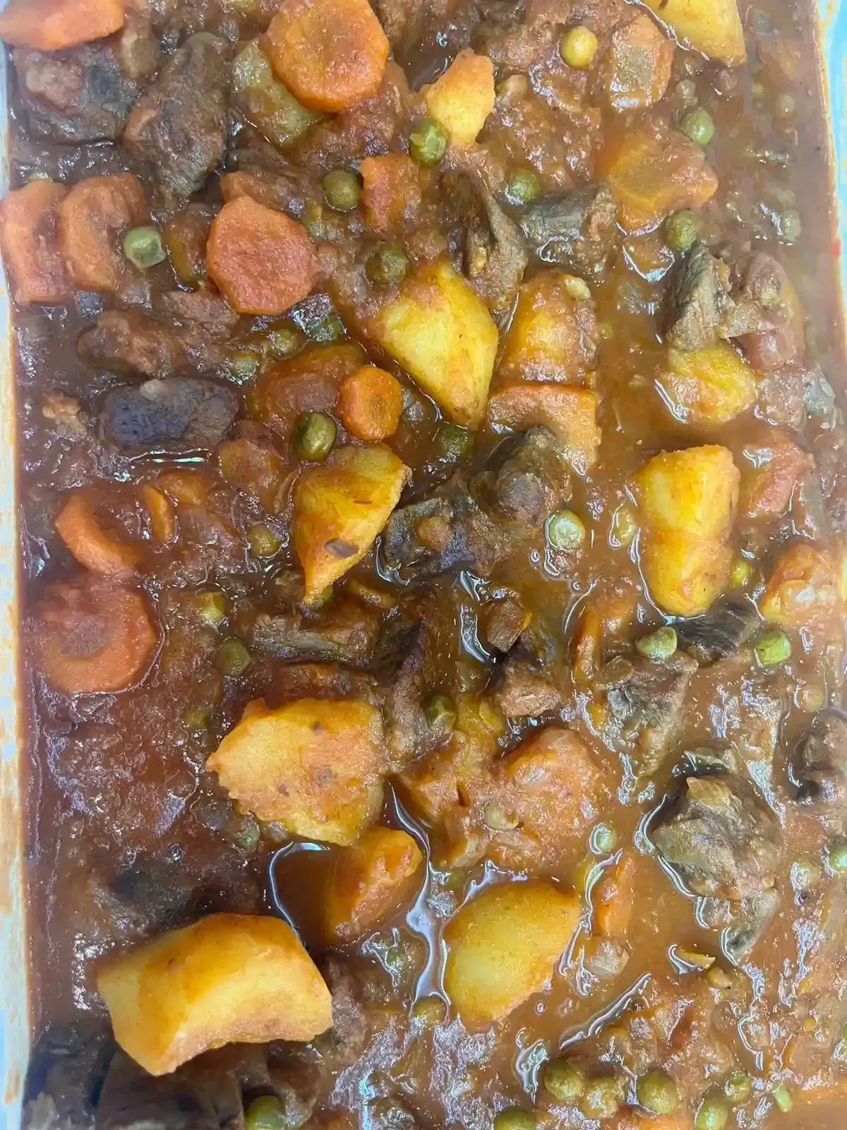 Primer plano de un guiso de verduras con trozos grandes, con zanahorias, patatas, guisantes y judías verdes en salsa marrón.