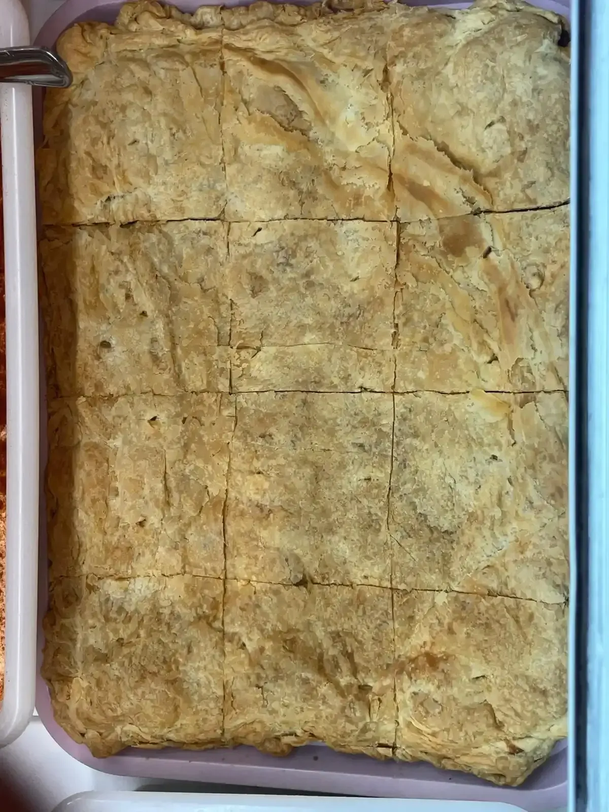 Un pastel rectangular horneado, de color marrón dorado, servido en un plato blanco, con líneas marcadas en la parte superior.