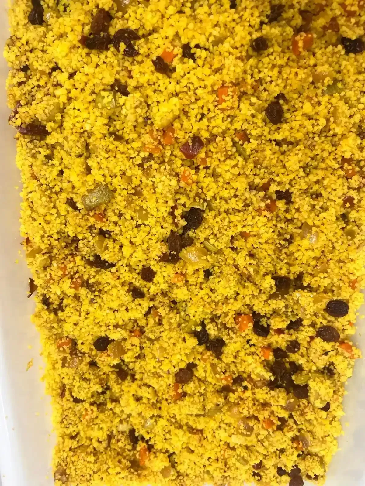 Cuscús amarillo con verduras y judías verdes esparcidas, primer plano en un plato.