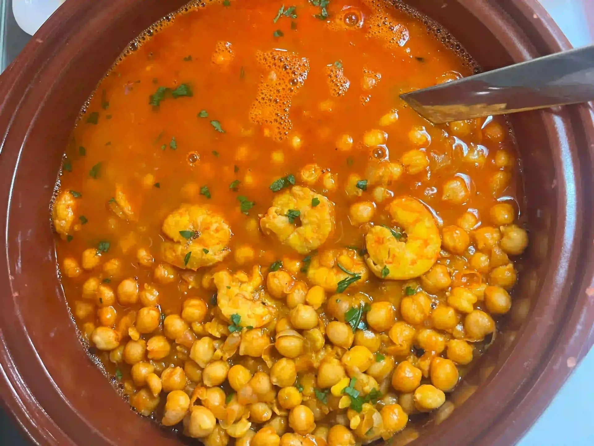 Bol de barro con curry de garbanzos, plátano en rodajas y una cuchara en salsa de naranja.