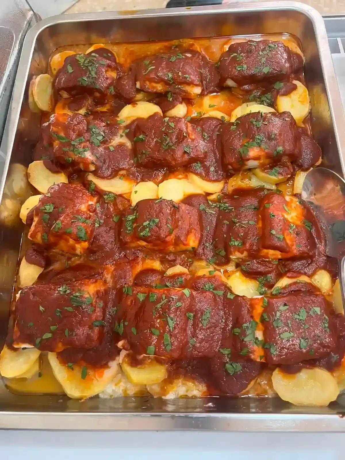 Bandeja de albóndigas en salsa sobre pasta, cubiertas con queso fundido y perejil picado.