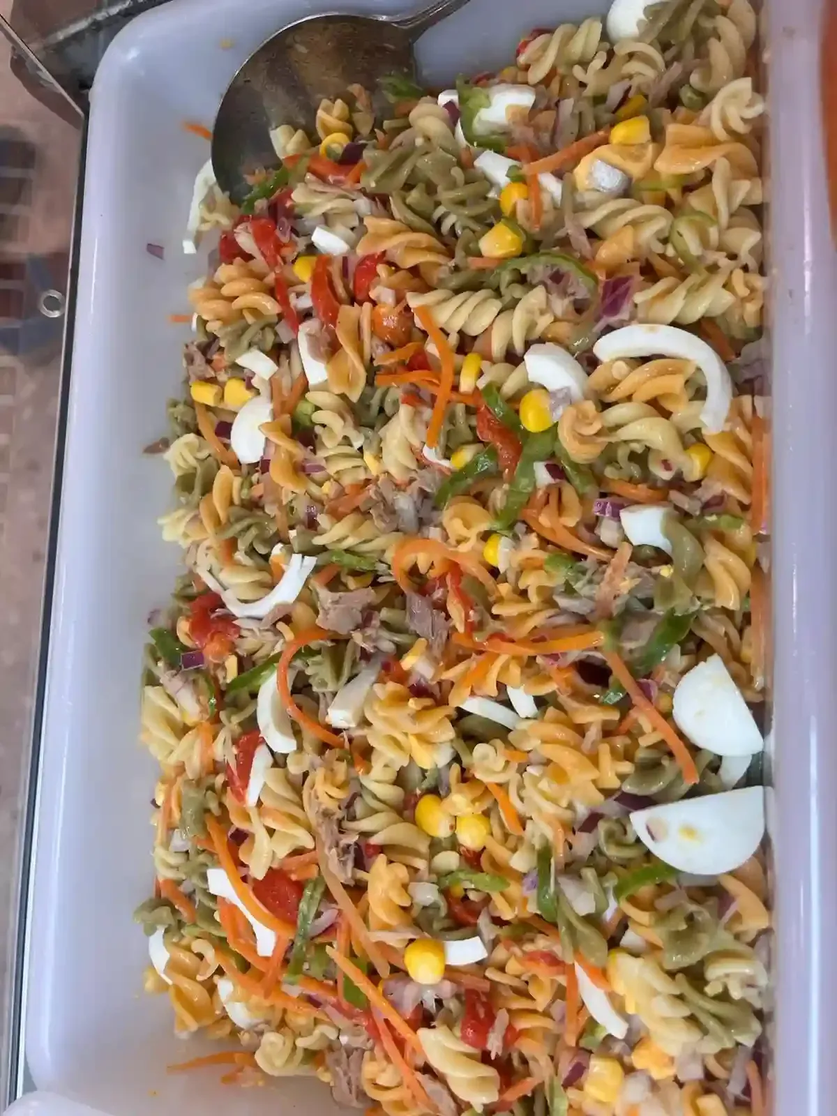 Bandeja de ensalada de pasta con fideos en espiral, verduras picadas y trozos de queso blanco.
