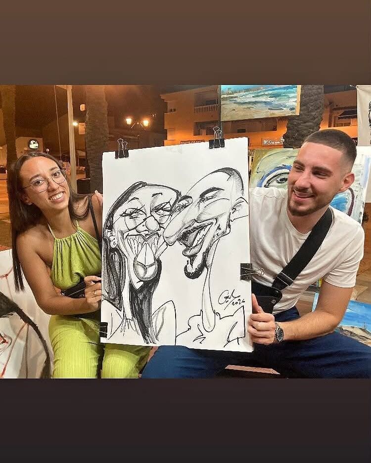 Dos personas sonriendo y sosteniendo un dibujo de caricatura en un evento en interiores.