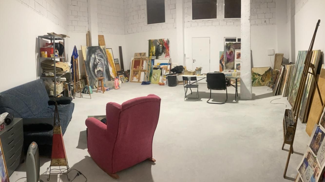 Estudio de arte con caballetes y coloridas pinturas abstractas sobre mesas de madera, paletas de pintura y pinceles a la vista.