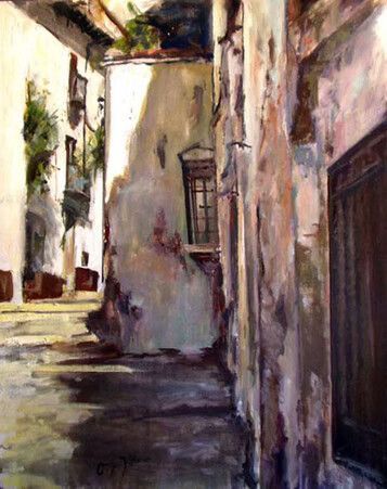 Un estrecho callejón soleado con paredes blancas desgastadas, sombras y una puerta de madera oscura.