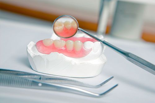 Un modelo de dentadura postiza con un espejo dental y pinzas sobre una mesa.