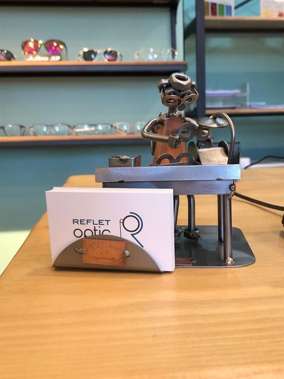 Sculpture en métal d'une personne portant des lunettes à un bureau avec des cartes de visite sur lesquelles est écrit REFLET OPTIC
