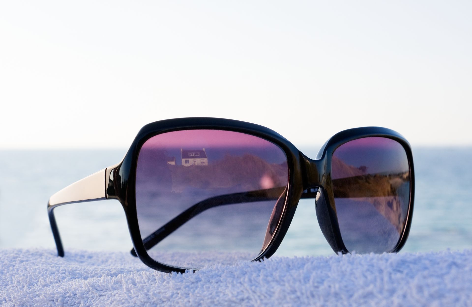 Des lunettes de soleil posées sur une serviette blanche, avec l'océan en arrière-plan.