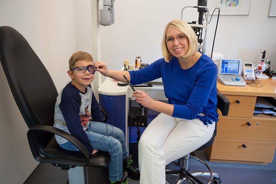 Junge mit Brille bei einer Augenuntersuchung, Arzt hält ein Testgerät in einer Praxis.