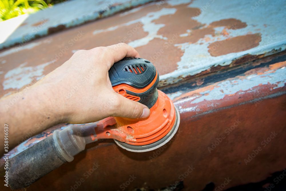 Une personne ponce un bateau rouillé avec une ponceuse.