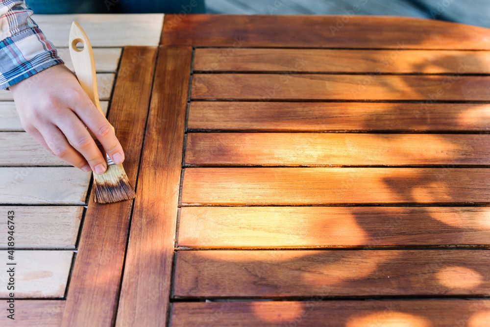 Une personne peint une table en bois avec un pinceau.