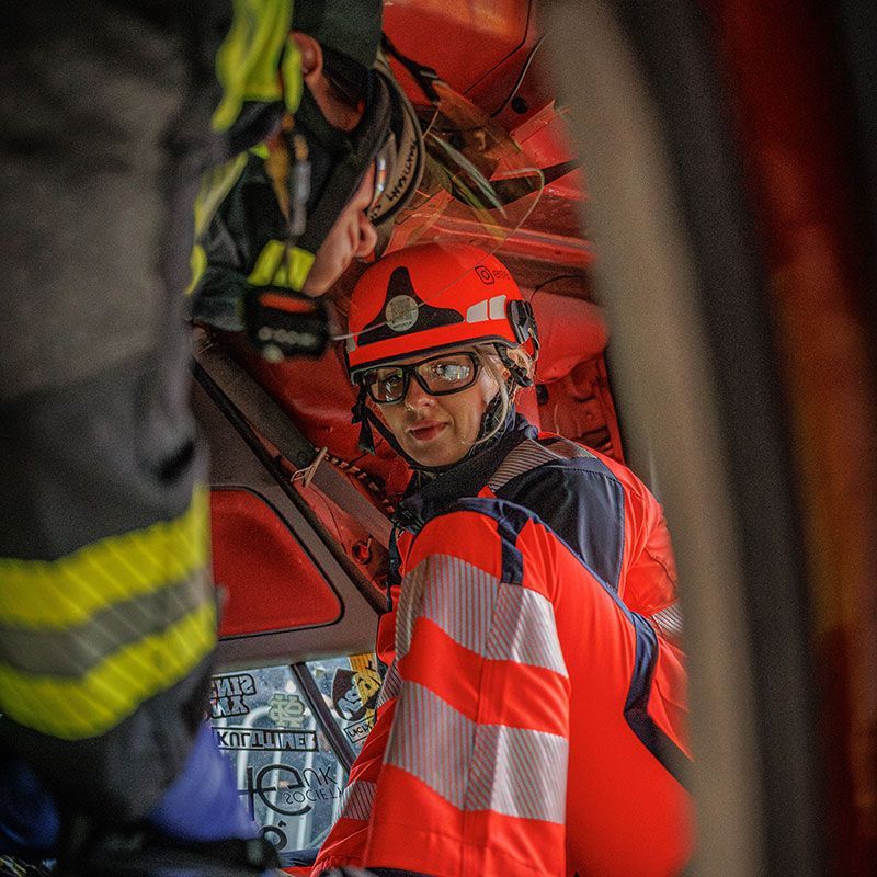 Feuerwehrmann mit rotem Helm und Warnweste in einem Rettungsfahrzeug, der in die Kamera schaut.