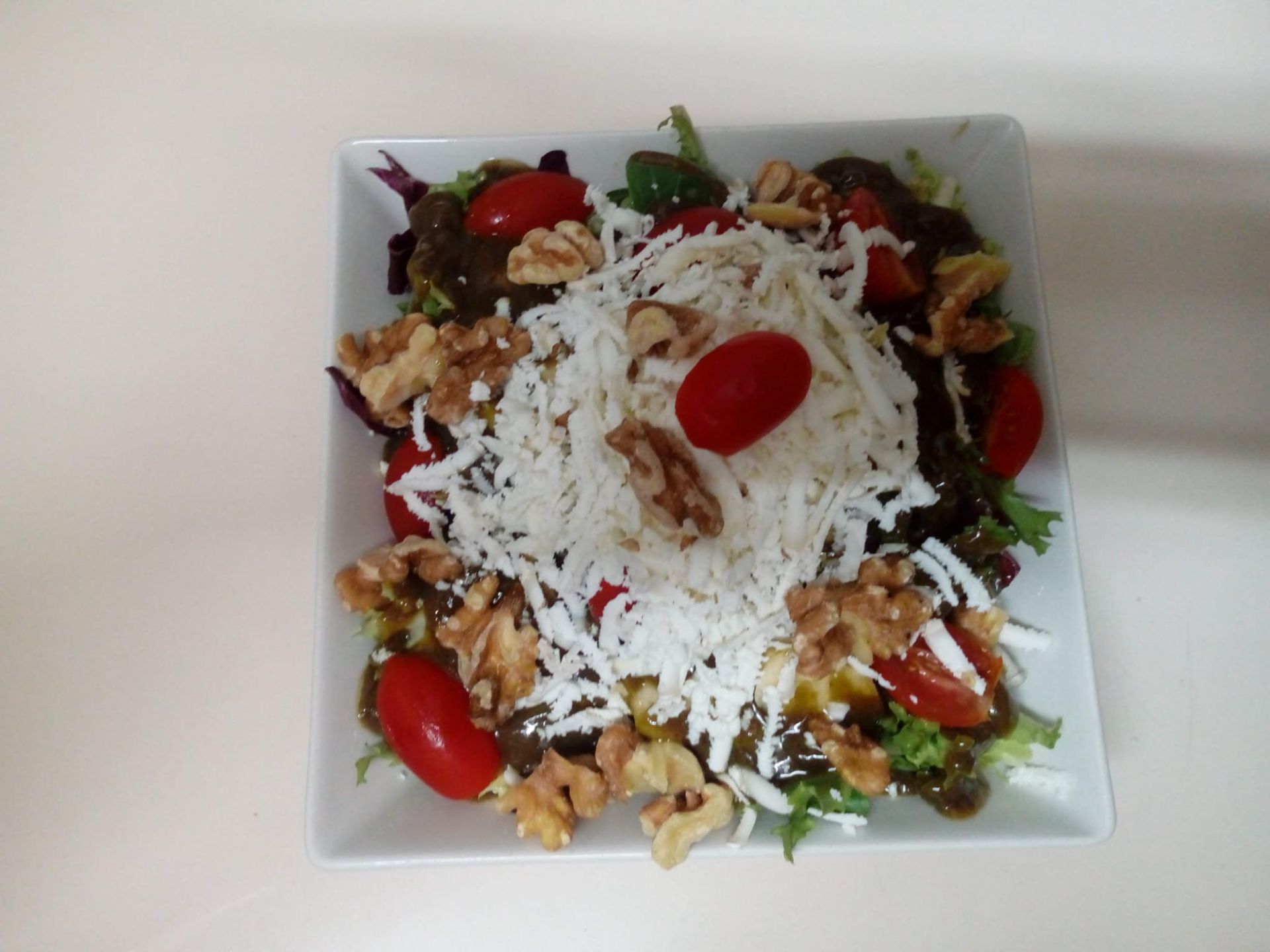 Una ensalada con tomates, nueces y queso en un plato blanco.