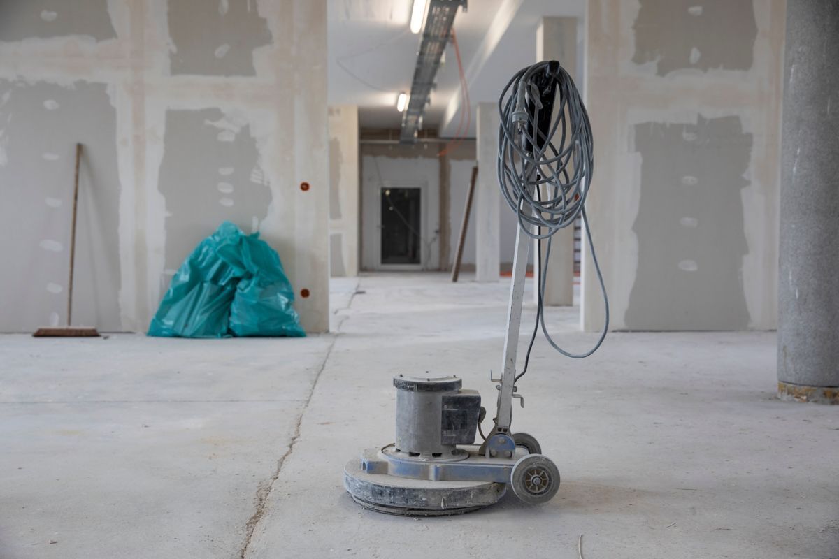 Eine Bodenschleifmaschine in einem im Bau befindlichen Gebäude, zwischen Gipskartonplatten und Müllsäcken.