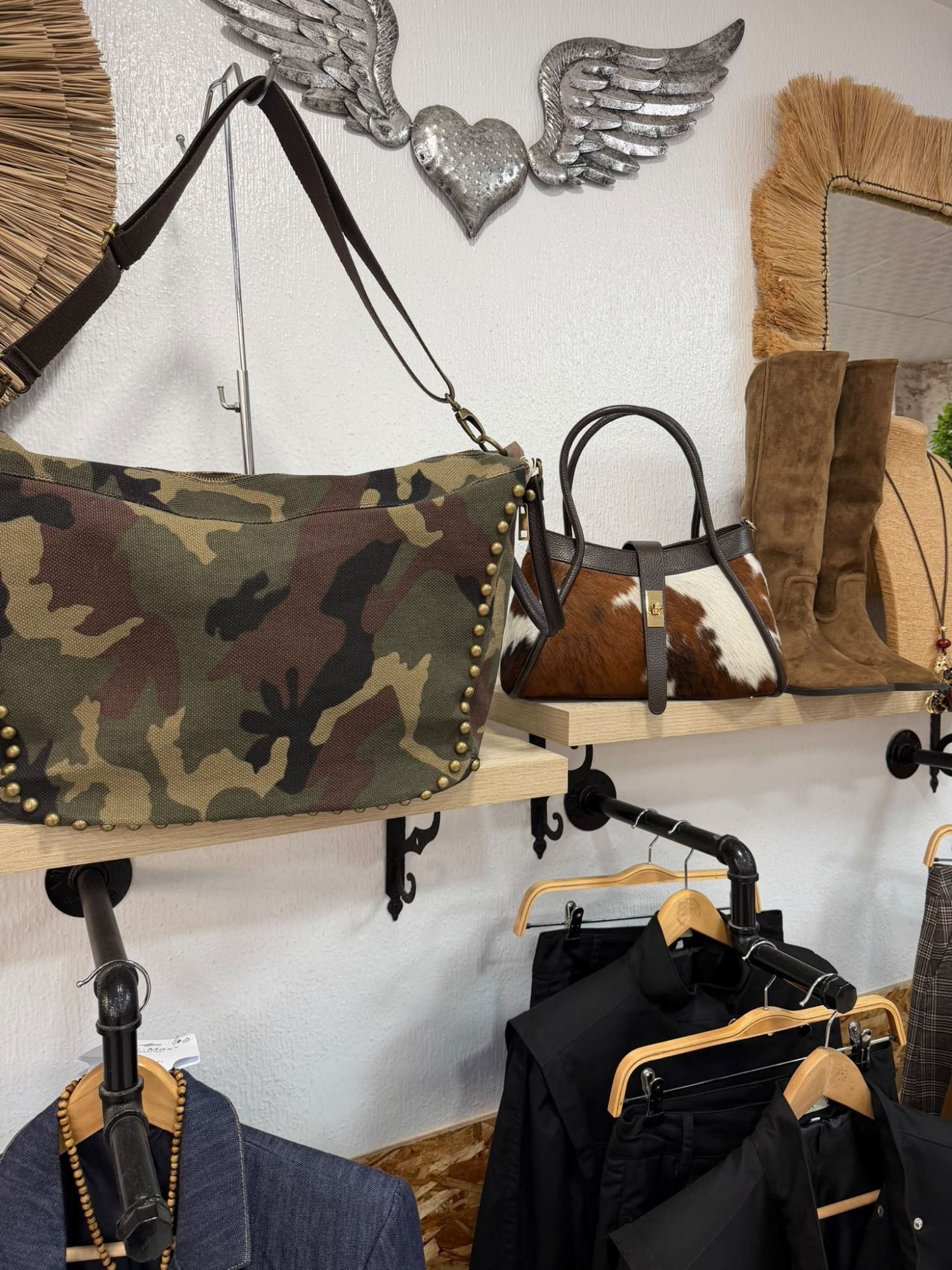 Bolsos y chaquetas expuestos en ganchos de pared en una boutique, incluidos bolsos de camuflaje y marrones.
