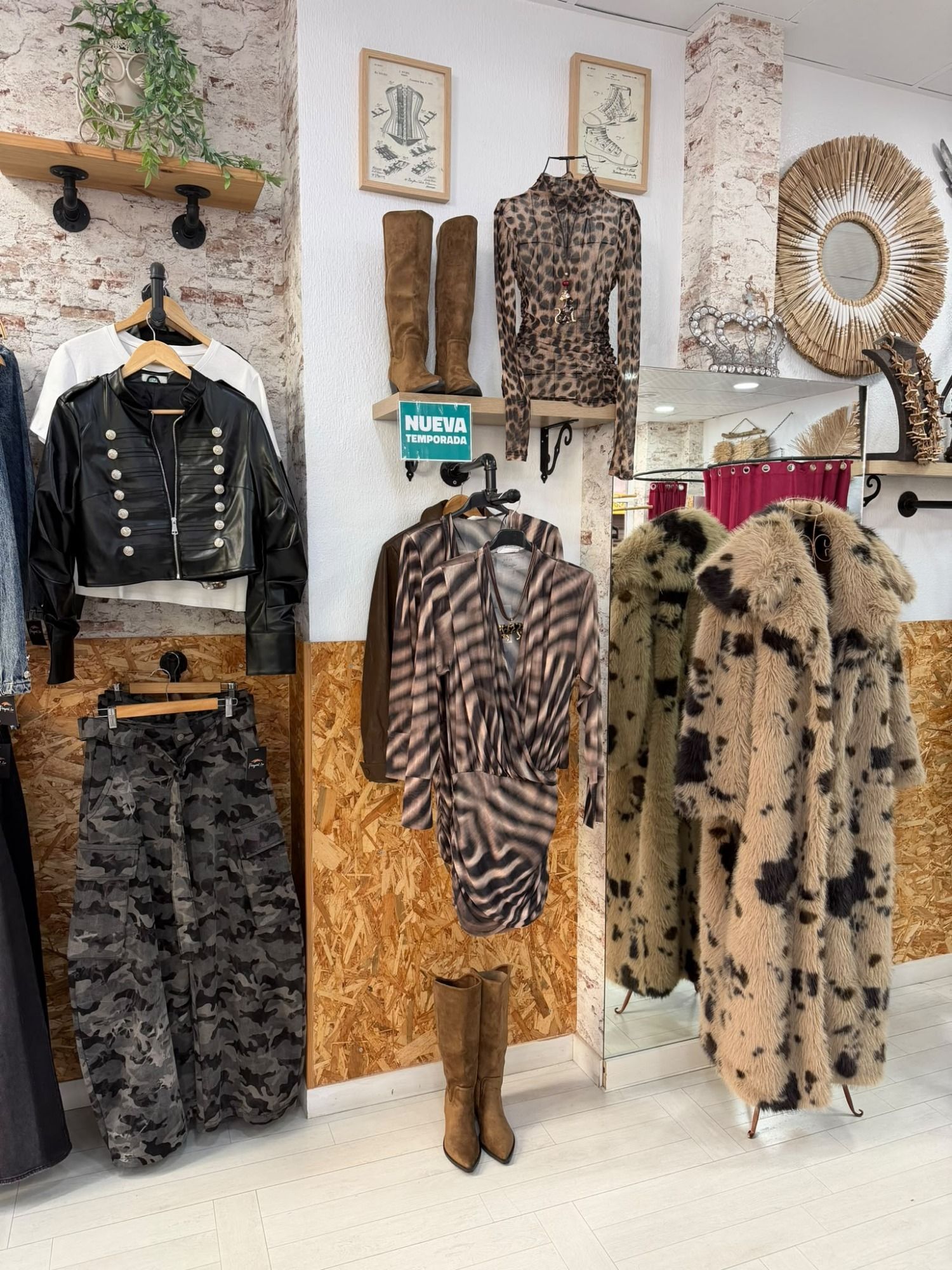 Escaparate de una boutique de ropa con abrigos, faldas, chaquetas y botas estampados, y decoración mural sobre una pared