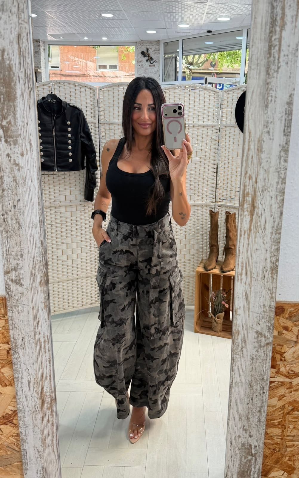 Selfi frente al espejo en una tienda de ropa, con un top negro y unos pantalones grises estampados.