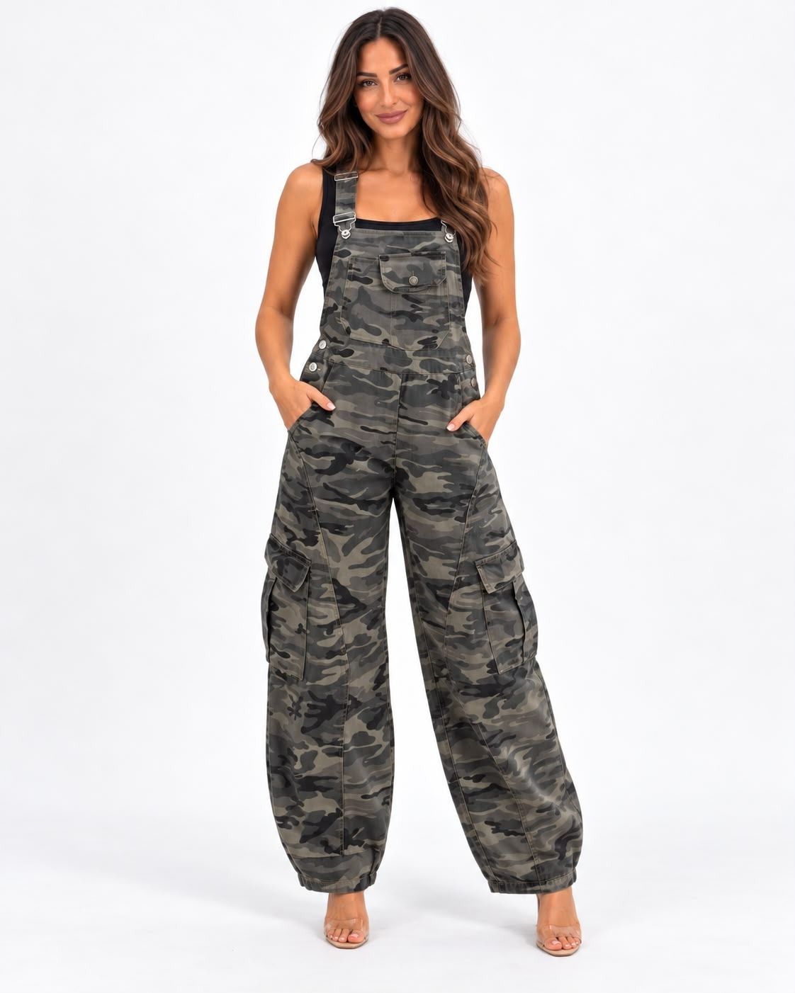 Mujer con un mono de camuflaje gris y pantalones, de pie frente a un fondo blanco con las manos en los bolsillos.