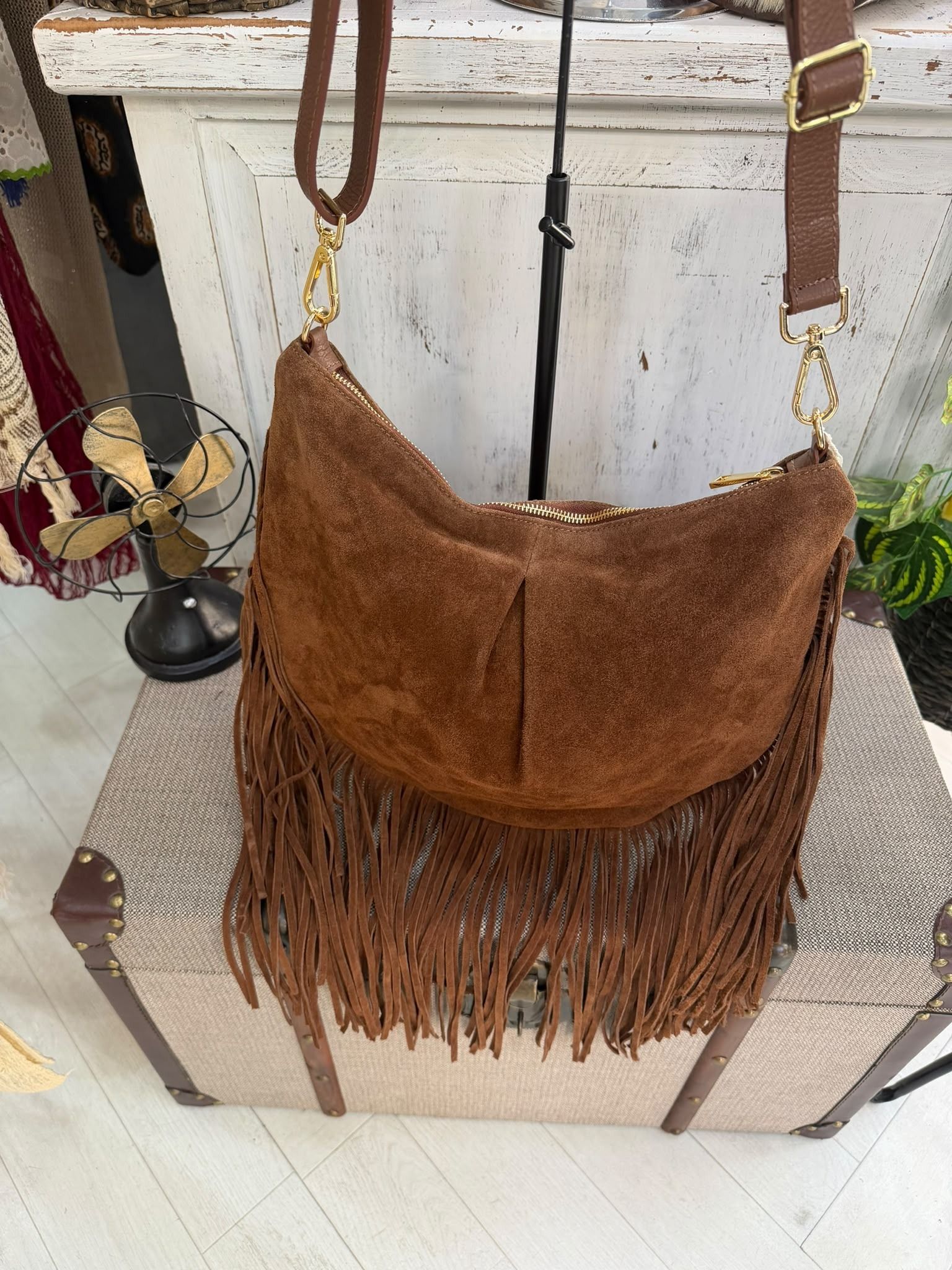 Bolso bandolera marrón de ante con flecos, colgado en una silla en un ambiente doméstico