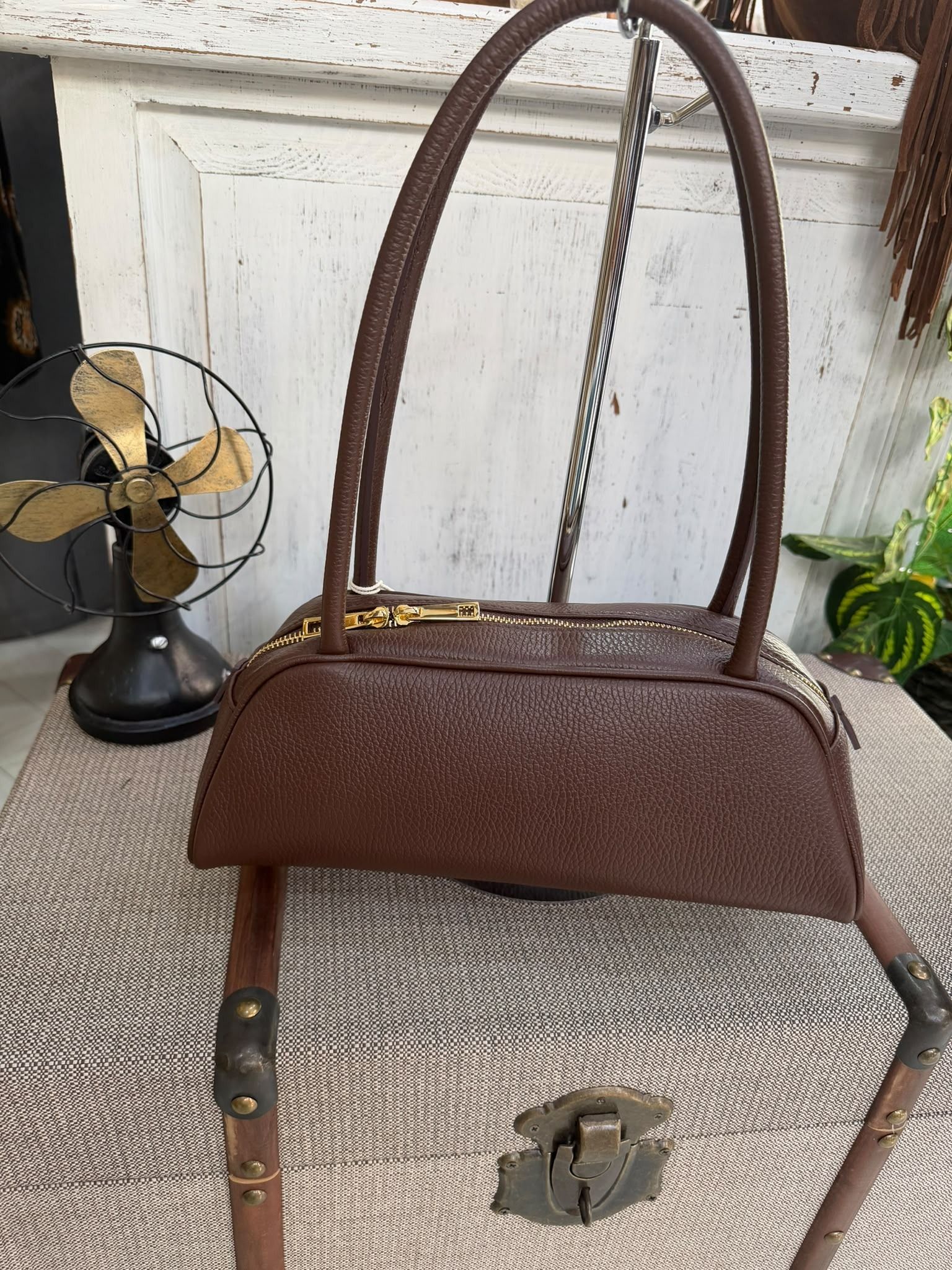 Bolso vintage marrón con cadena para colgar, sobre una silla de mimbre en el interior