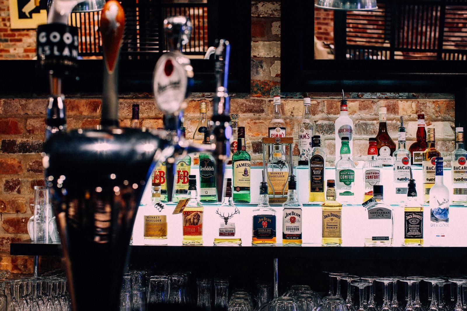 Bar with liquor bottles, beer taps, and glasses; brick wall background.