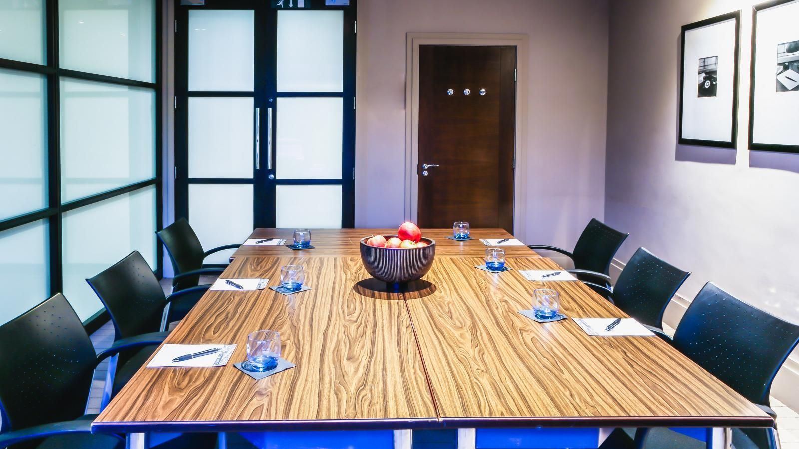 Conference room with large wooden table, chairs, and decorative fruit bowl.