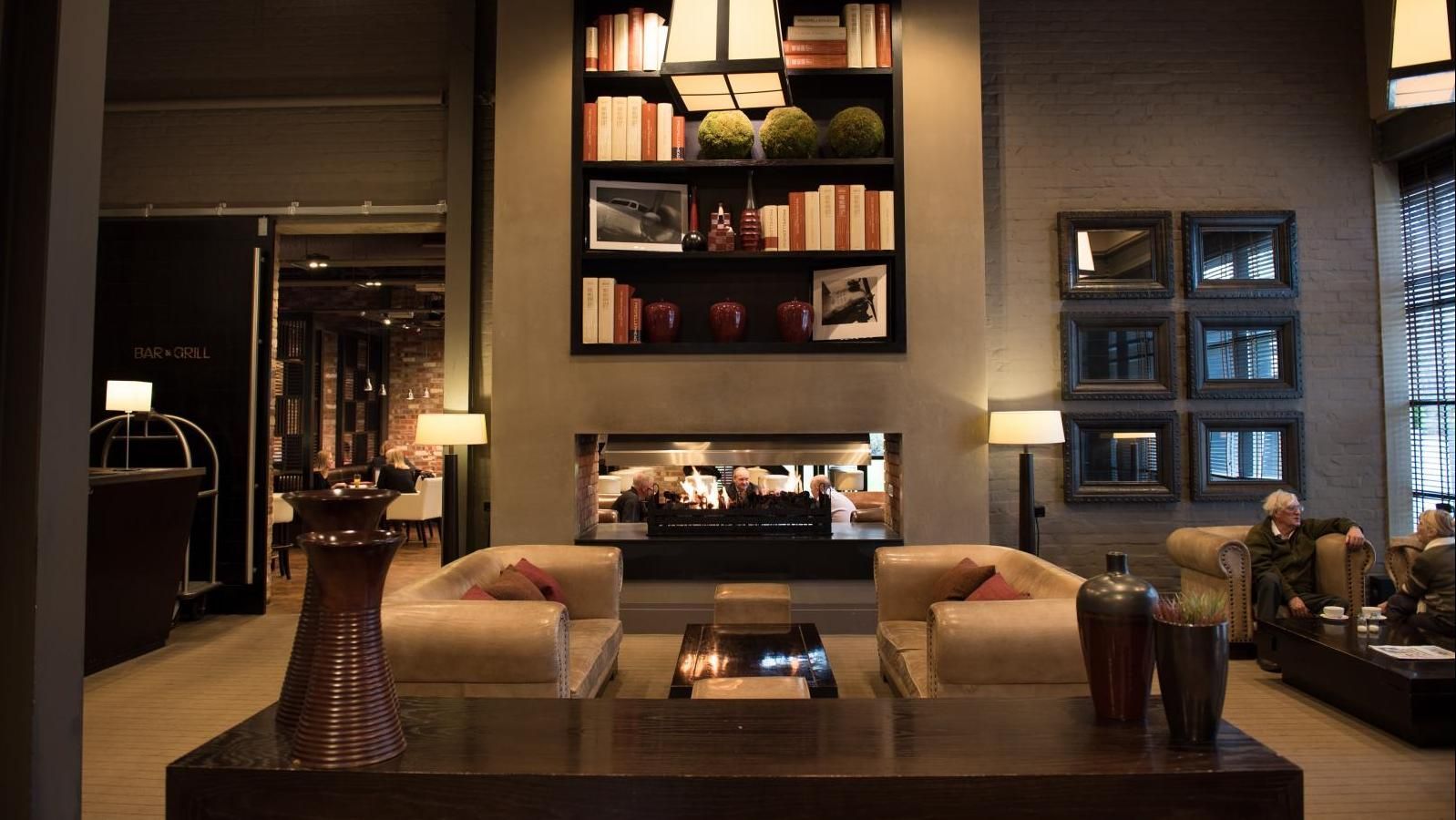 Lobby with fireplace, bookshelves, and seating. Warm colors, natural light. People are present.