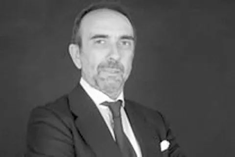 Un hombre con traje y corbata está de pie con los brazos cruzados.